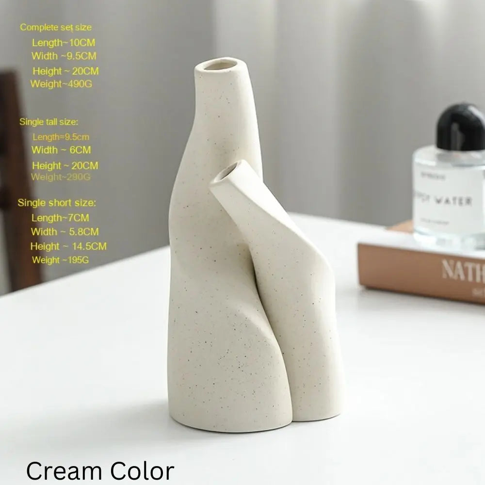 Cream-colored ceramic vases with a unique, modern design, displayed on a table with decorative items in the background.
