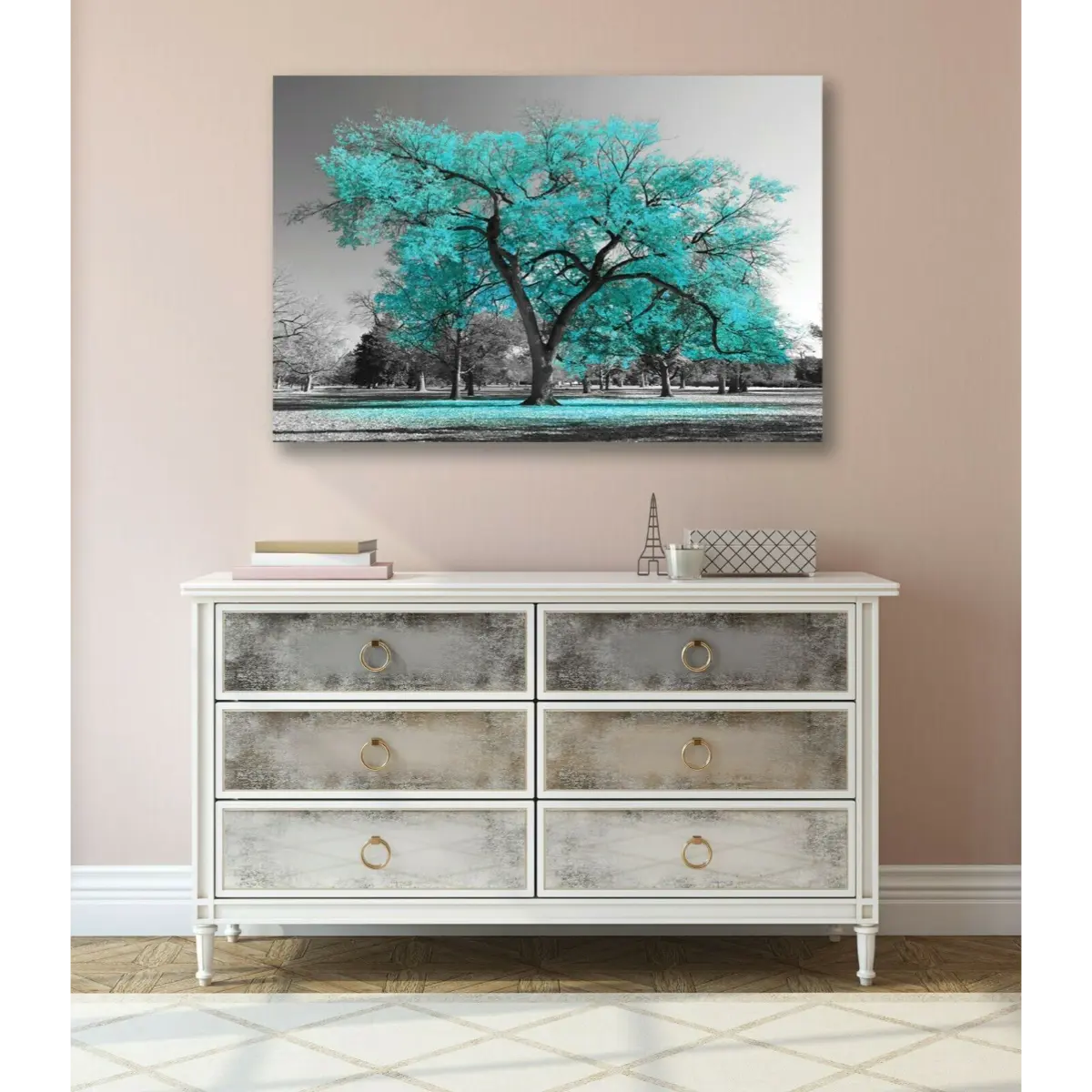 A serene interior featuring a white dresser with glass-front drawers, a teal tree artwork above, and a light pink wall backdrop.