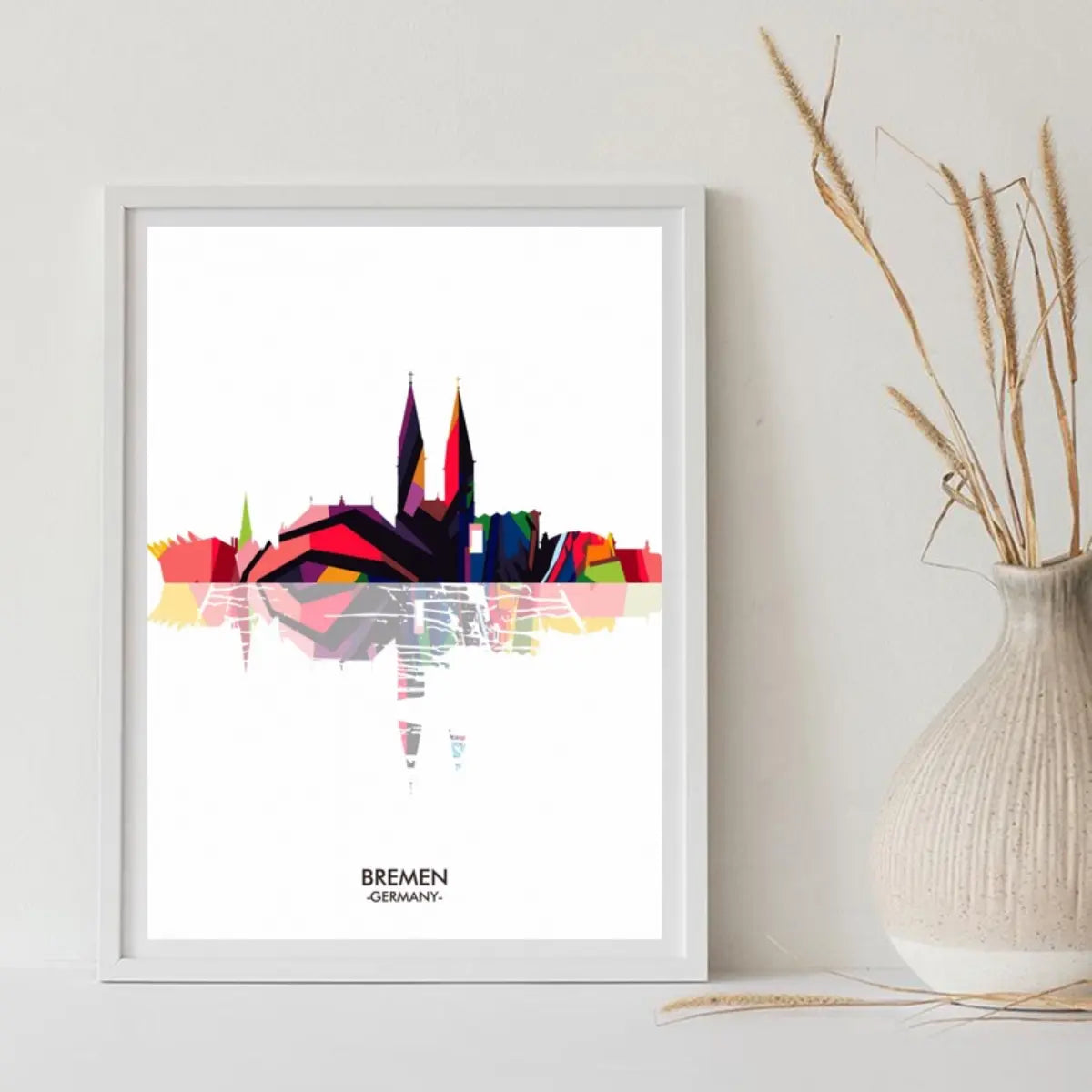 Colorful geometric illustration of Bremen's skyline in a white frame, featuring prominent towers and reflections on water.