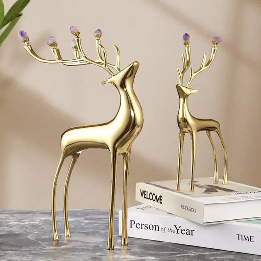 Two elegant golden deer sculptures with amethyst-topped antlers, displayed on stacked books against a neutral background.