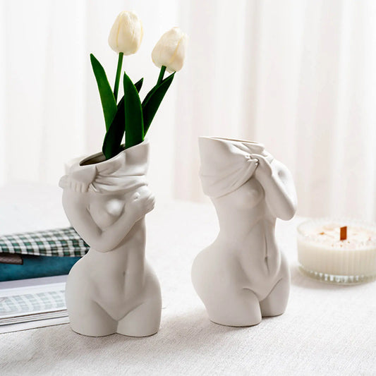 Two elegant white vases shaped like female forms, adorned with faux tulips, set against a soft fabric background.
