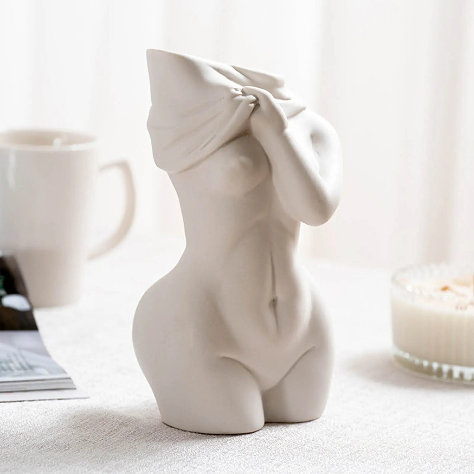 A minimalist white ceramic vase of a woman with a covered head, showcasing elegant curves, against a soft, natural background.