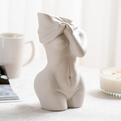 A minimalist white ceramic vase of a woman with a covered head, showcasing elegant curves, against a soft, natural background.