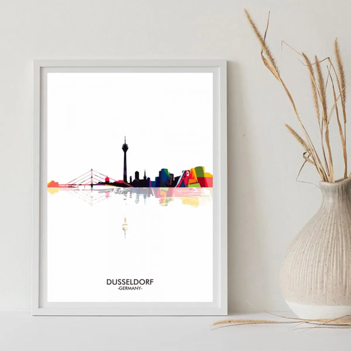 Colorful silhouette of Düsseldorf's skyline, featuring iconic buildings and the Rhine Tower, framed and displayed on a shelf.