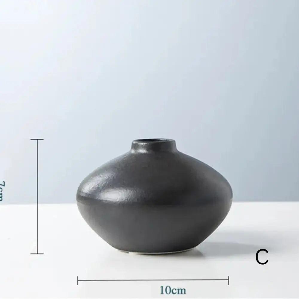 A sleek black ceramic vase with a rounded base and narrow neck, measuring 10cm in diameter and 7cm in height, on a light background.
