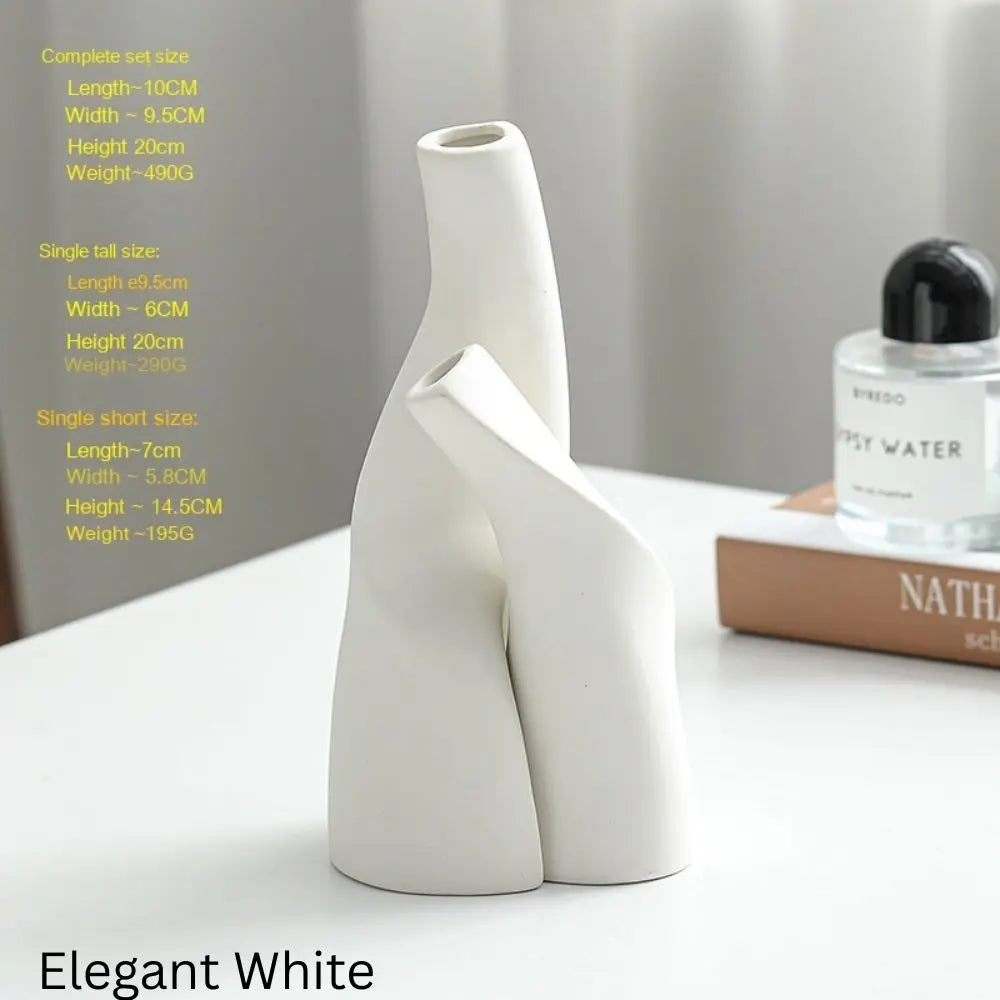 White ceramic vase with a unique, abstract design, displayed on a table with a perfume bottle and a book in the background.