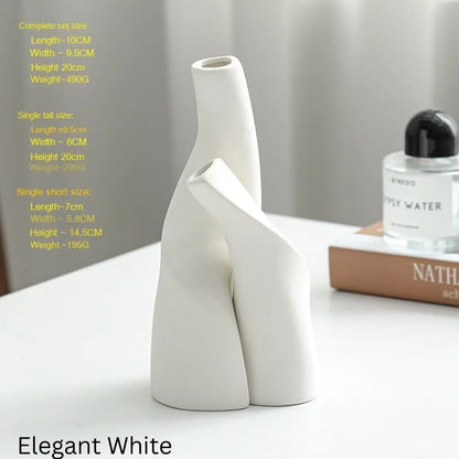 White ceramic vase with a unique, abstract design, displayed on a table with a perfume bottle and a book in the background.