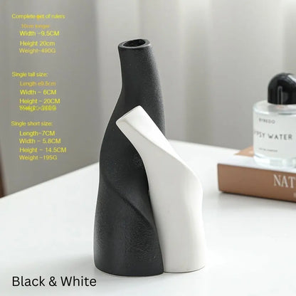 A stylish black and white ceramic vase with curved designs, accompanied by a fragrance bottle and a magazine on a table.