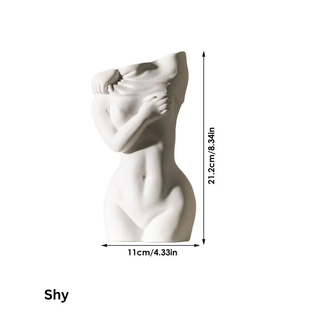 A white sculptural vase of a shy woman covering her torso, measuring 21.2cm tall and 11cm wide.