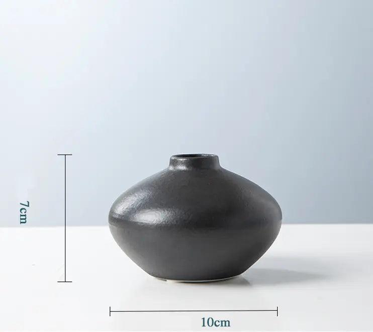A smooth, black ceramic vase with a rounded shape, measuring 7 cm in height and 10 cm in diameter, against a soft blue background.
