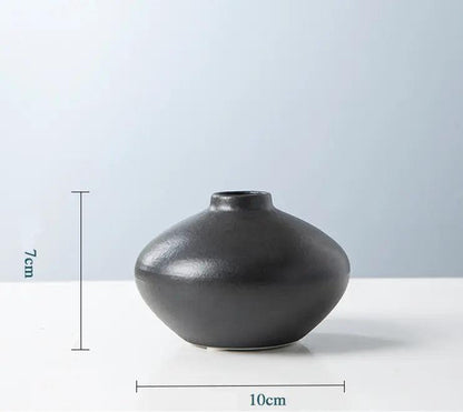 A smooth, black ceramic vase with a rounded shape, measuring 7 cm in height and 10 cm in diameter, against a soft blue background.