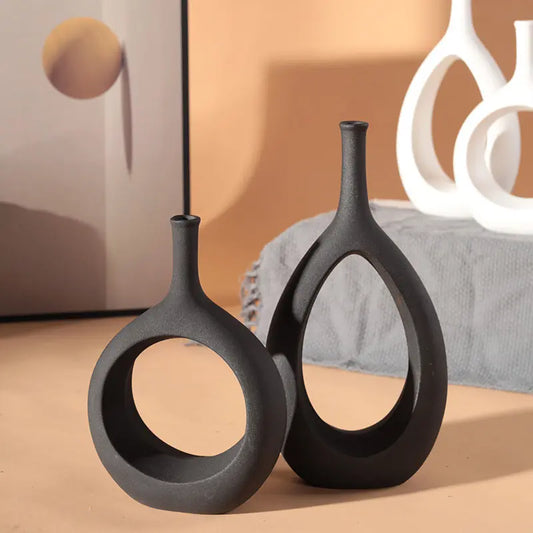 Two modern black vases in unique shapes, placed on a textured surface with a minimalist wall art piece in the background.