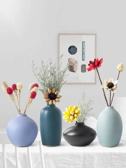 4 decorative vases with colorful flowers and greenery, set against a light wall with a geometric artwork above.