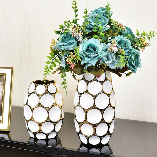 Elegant vases in black and white with gold accents, adorned with lush teal roses and green foliage, displayed on a sleek surface.