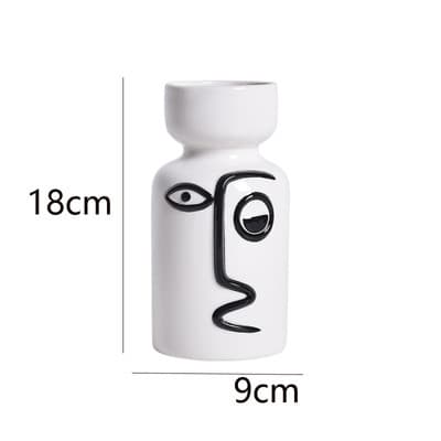 A white ceramic vase with a minimalist face design, measuring 18cm tall and 9cm wide, featuring black line art accents.